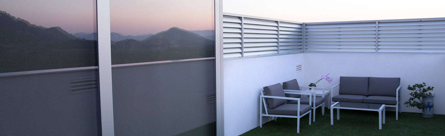 Ventanal con acceso a terraza junto a una celosía fija realizados en aluminio anonizado natural